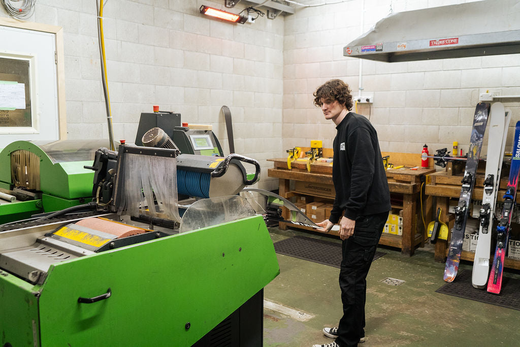 Technician feeding a ski into the Wintersteiger base grinder in the Racers Edge Wānaka NZ workshop
