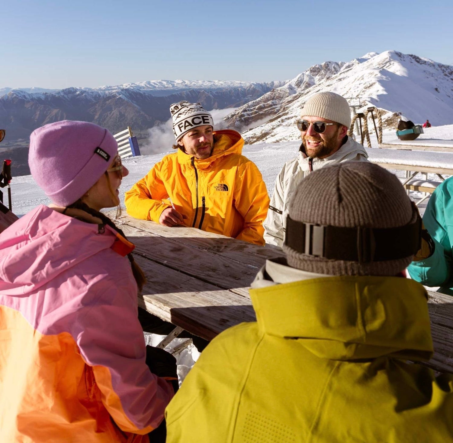 Group of skiers and snowboarders socialising at a picnic table on a ski field in Wānaka