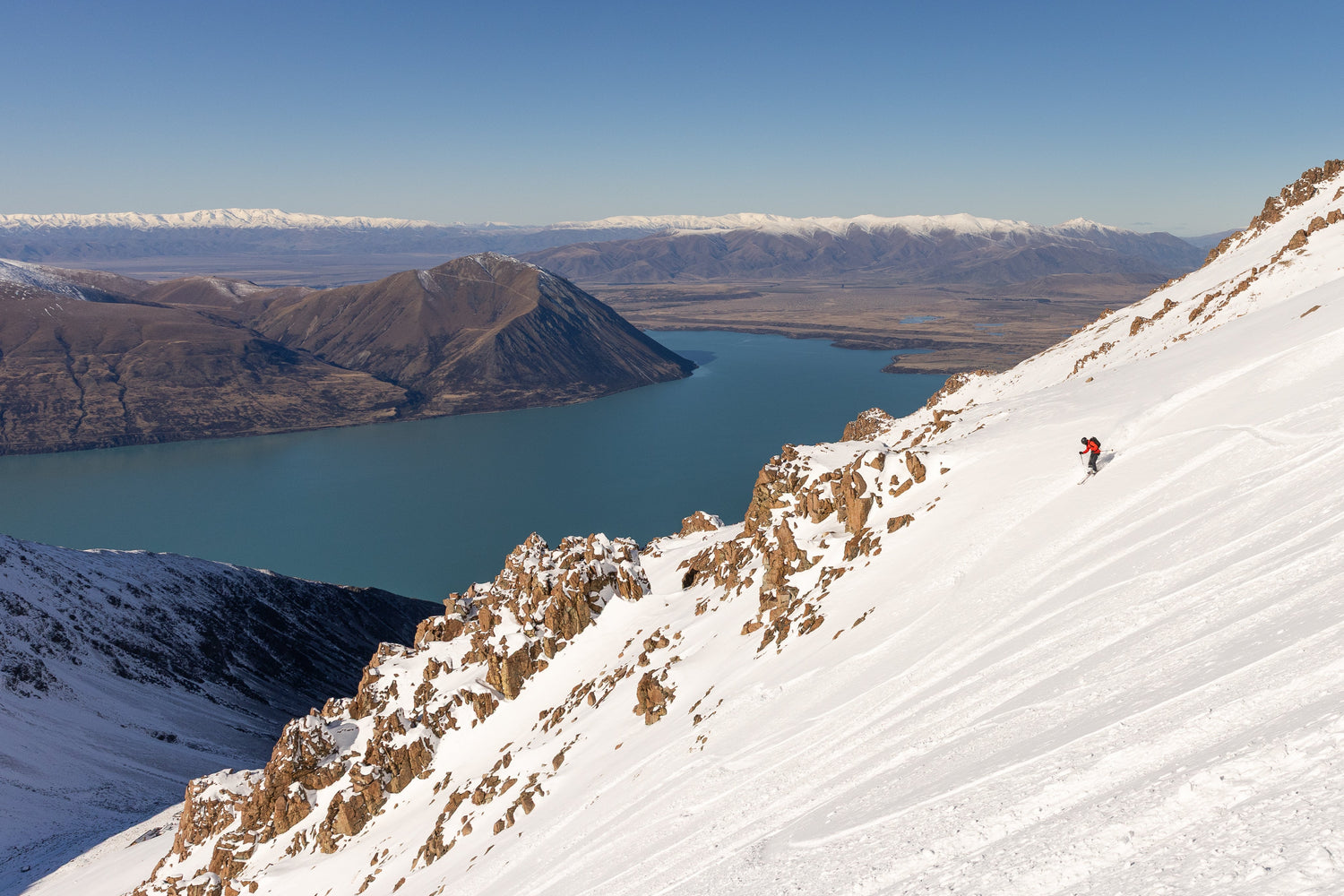 Backcountry skier descending a steep snowy face high above Lake Ohau