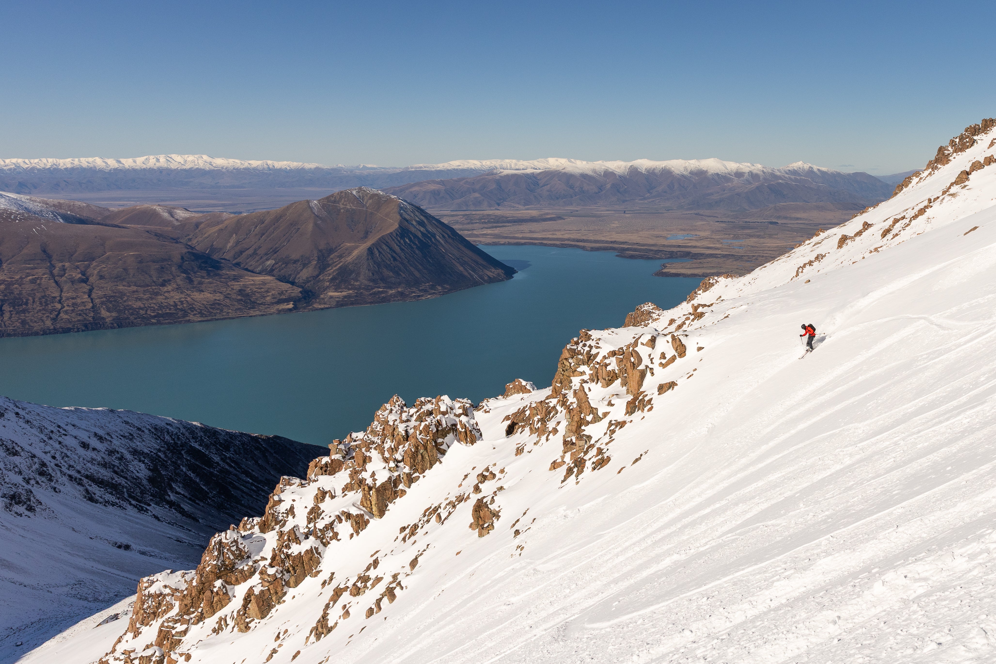 Backcountry skier descending a steep snowy face high above Lake Ohau