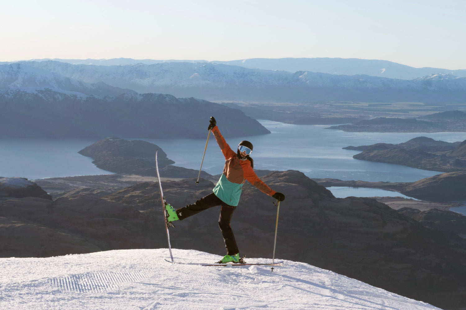 Skier posing on a summit high above Lake Wānaka with mountains stretching into the distance