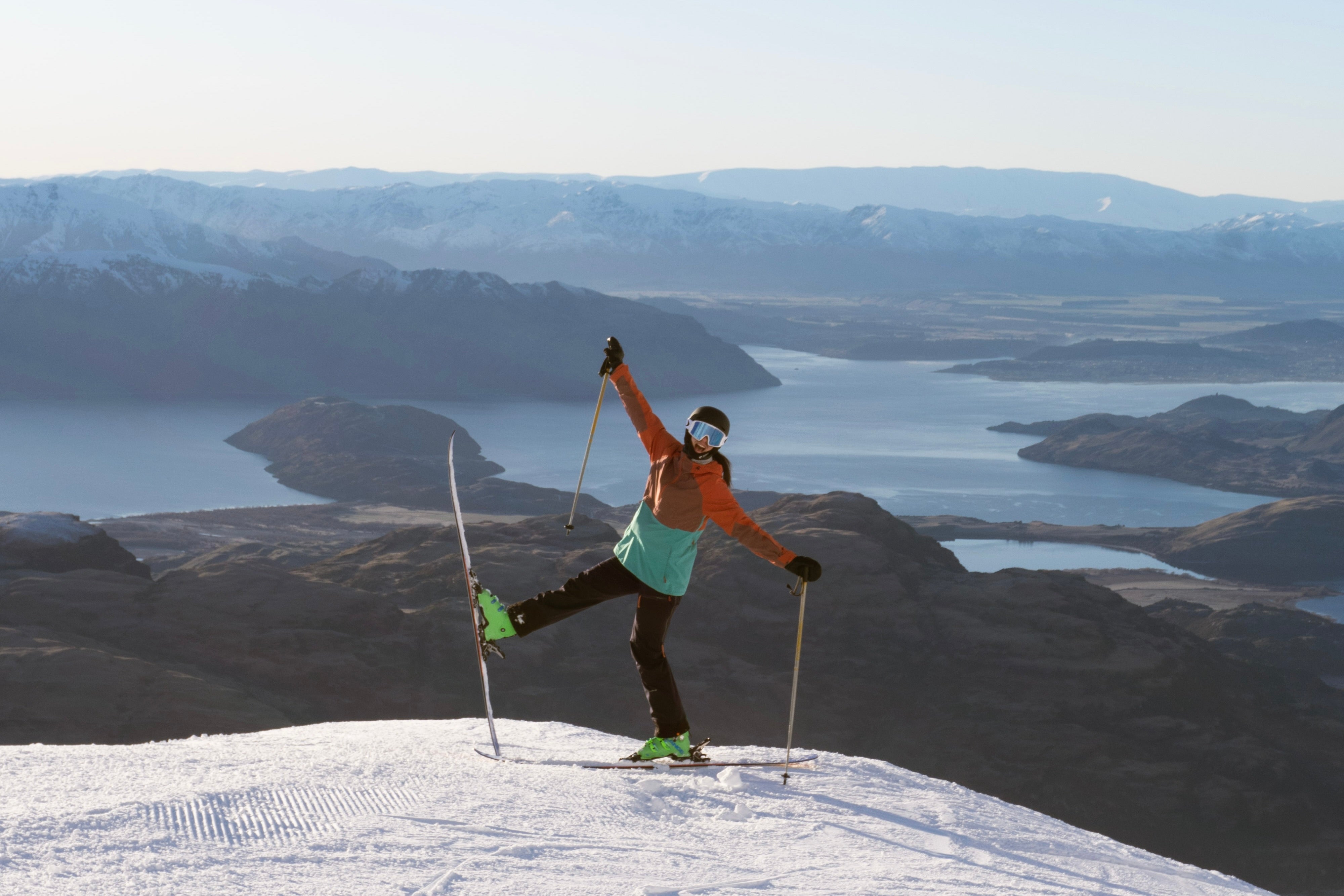 Skier posing on a summit high above Lake Wānaka with mountains stretching into the distance